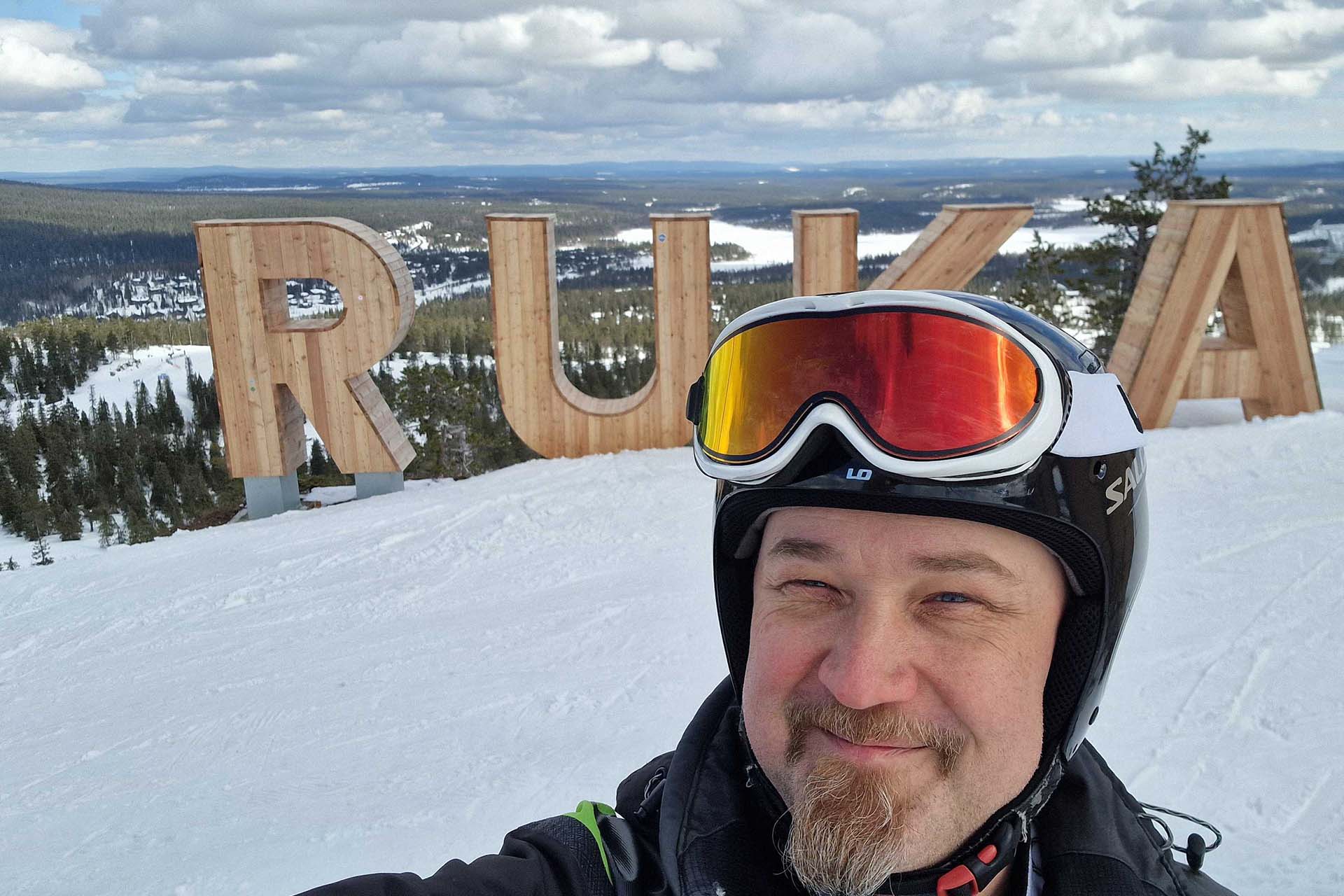  A smiling man with the Ruka sign and a snowy landscape in the background
