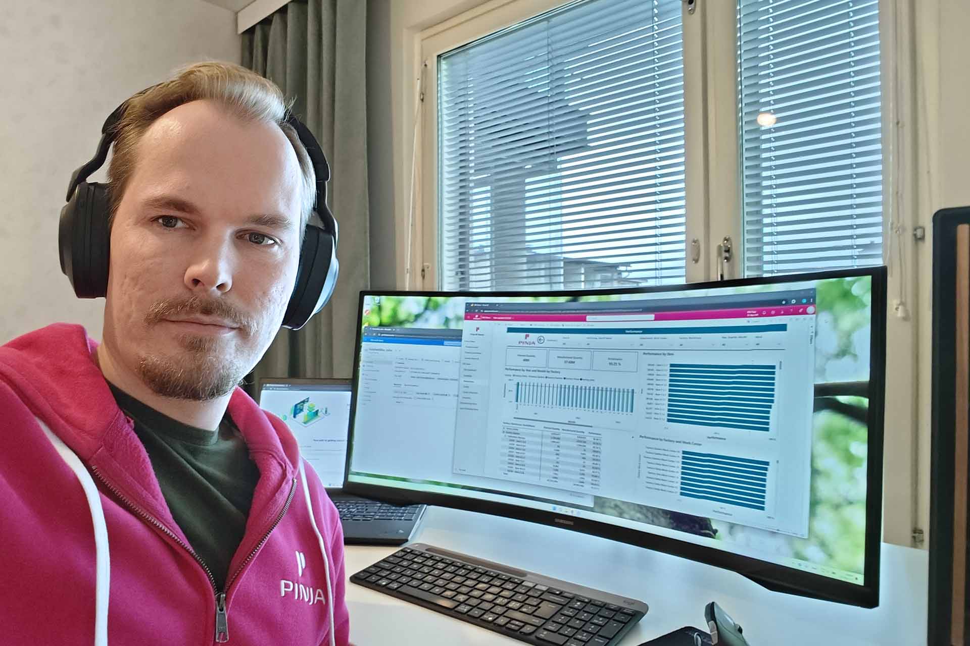  A man in a fuchsia hoodie at a computer with reports on the screen