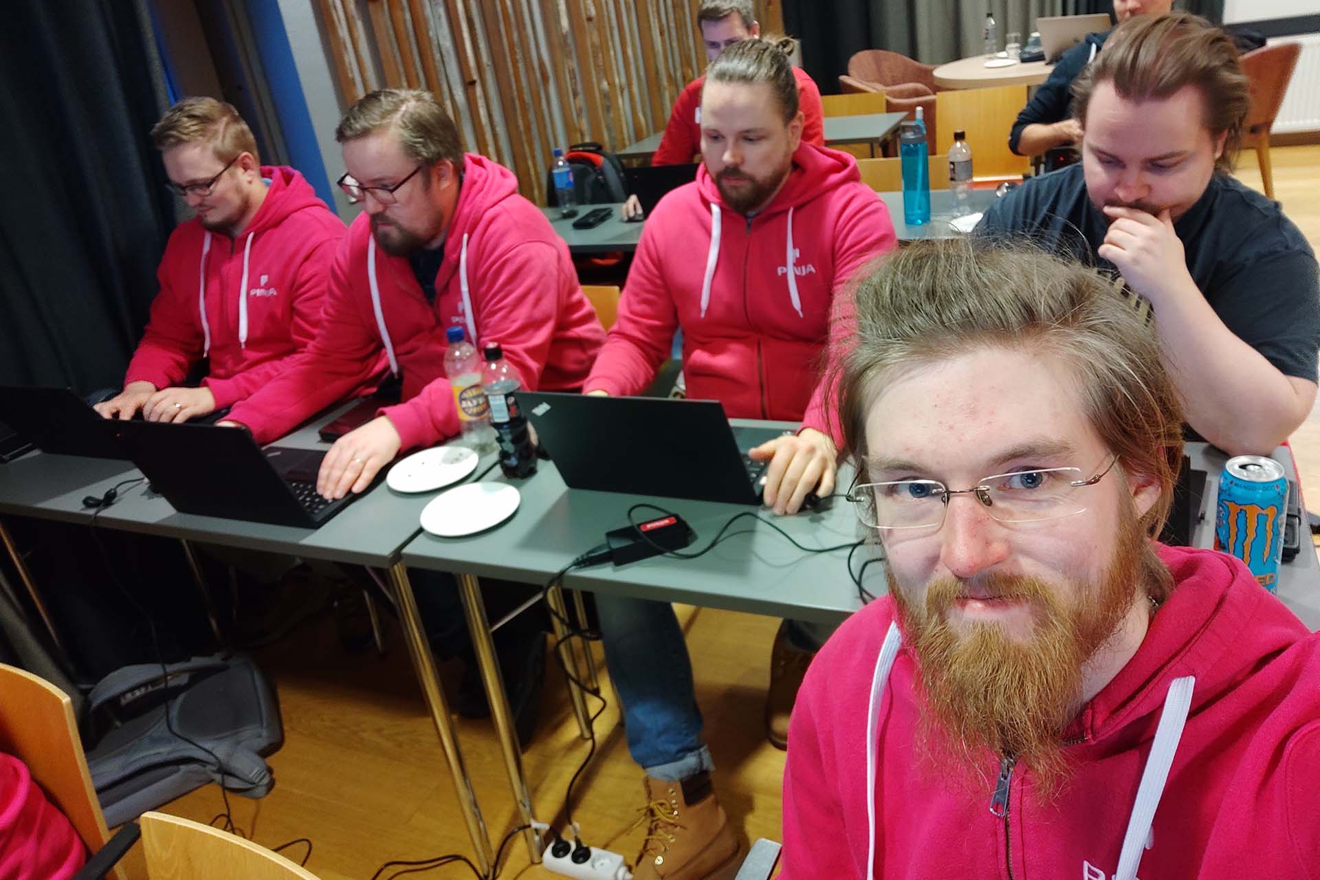 Men in fuschia hoodies sitting on their laptops in a classroom