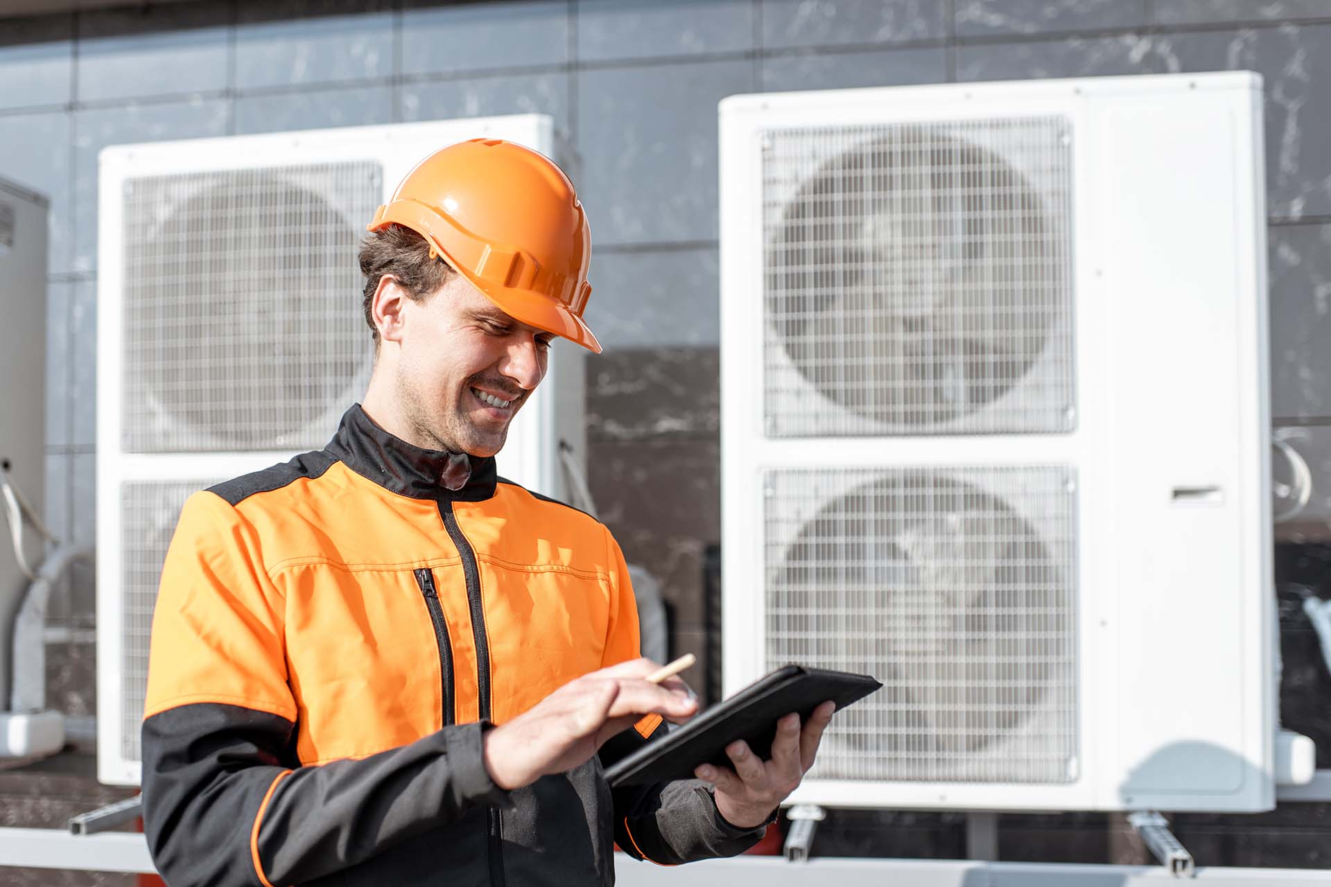 A helmeted man using a tablet in the foreground of ventilation equipment