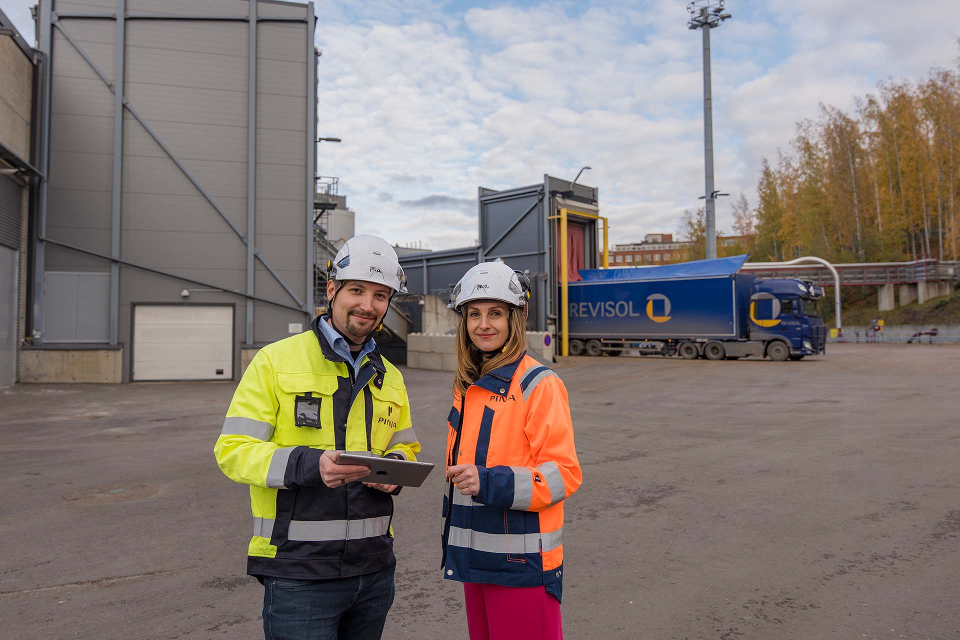 A man and a woman in work equipment in the yard of an energy plant, holding a tablet