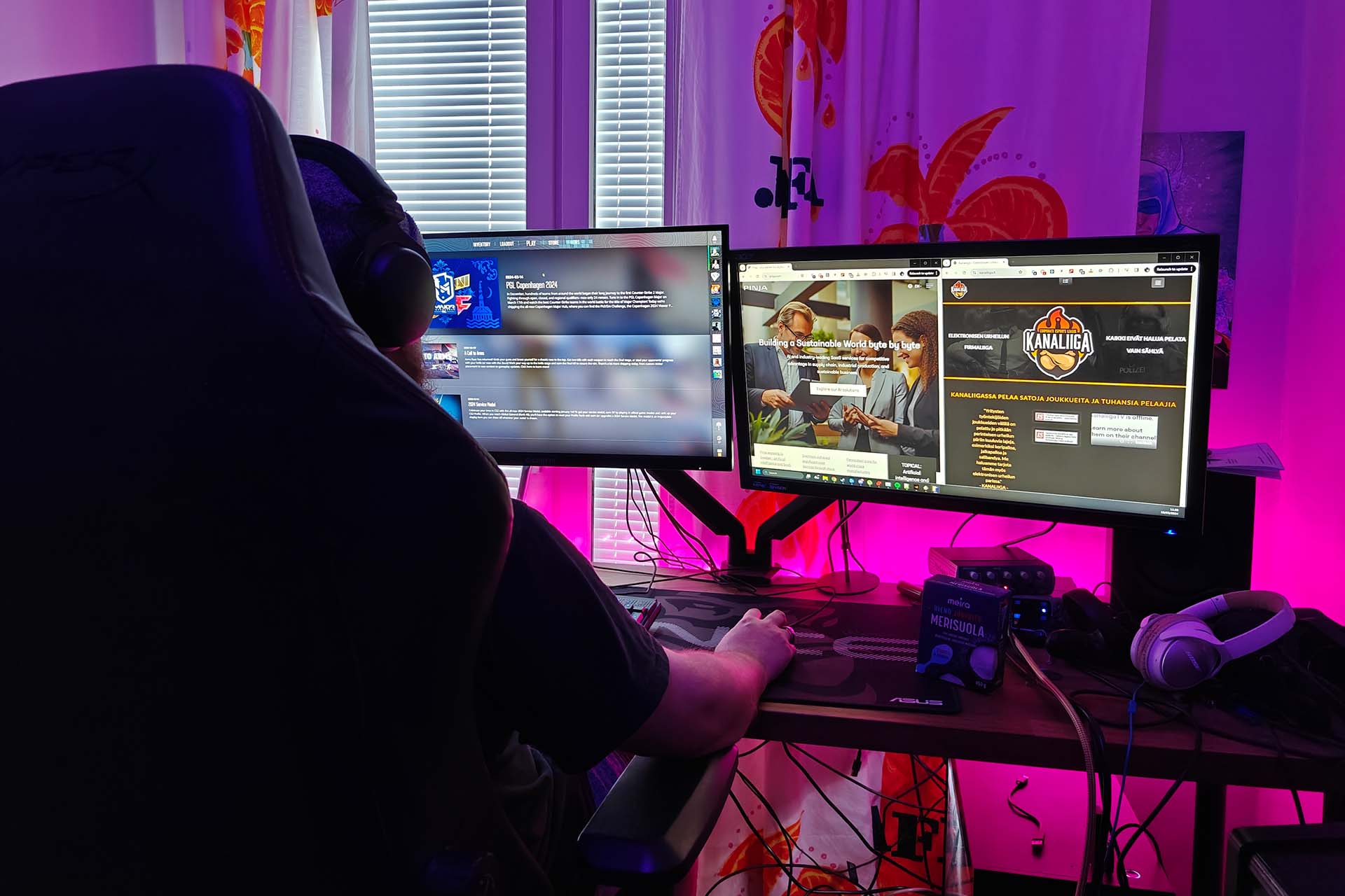  A man with a beanie sitting by two screens with his back to the camera.