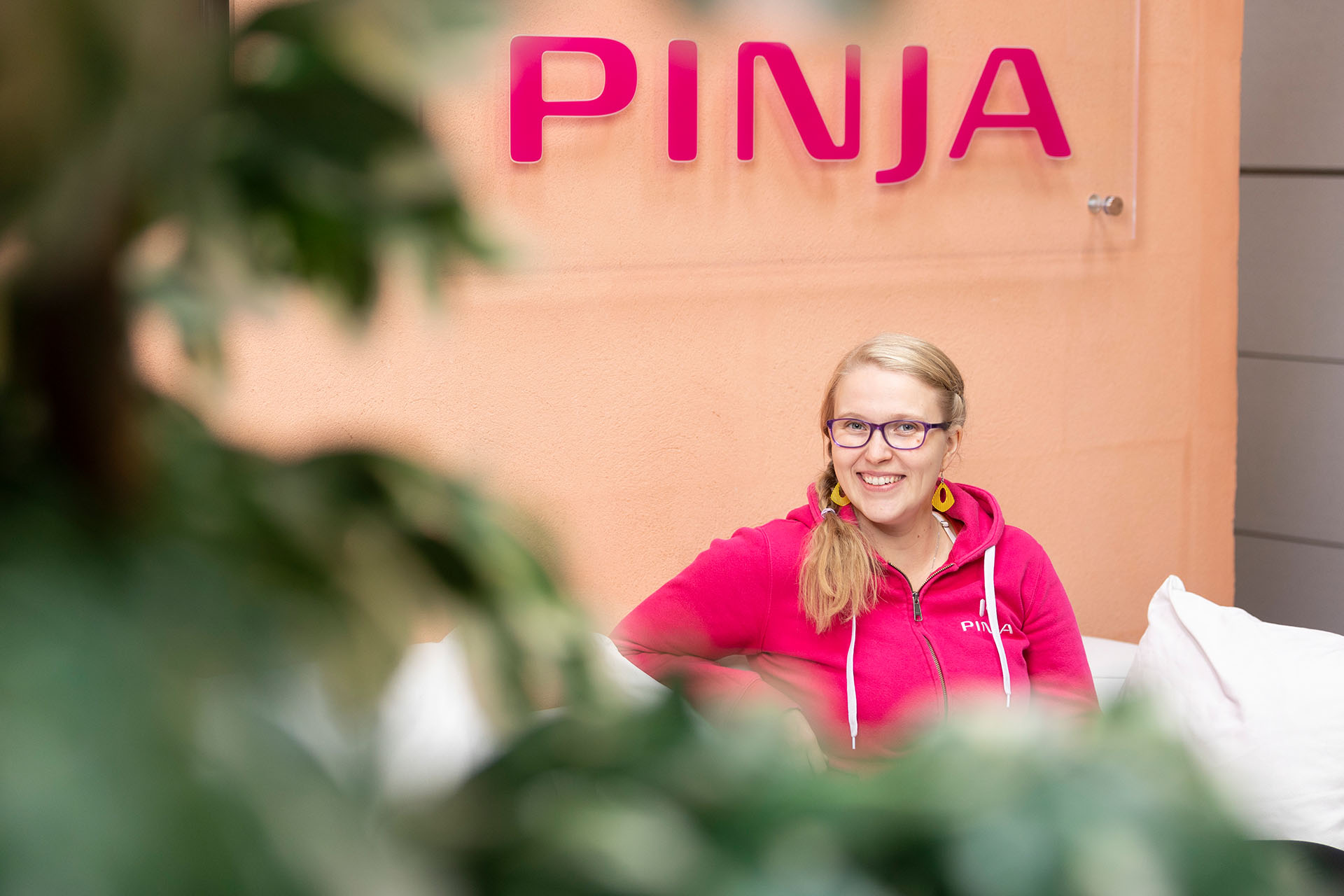Service desk employee Paula Huuskonen wearing a Pinja hoodie sitting on a white sofa under a Pinja sign