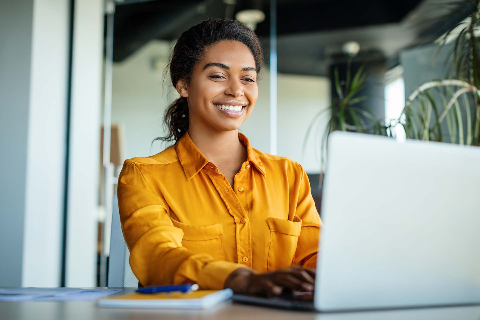 Tummatukkainen nainen hymyilee kannettavalle tietokoneelleen