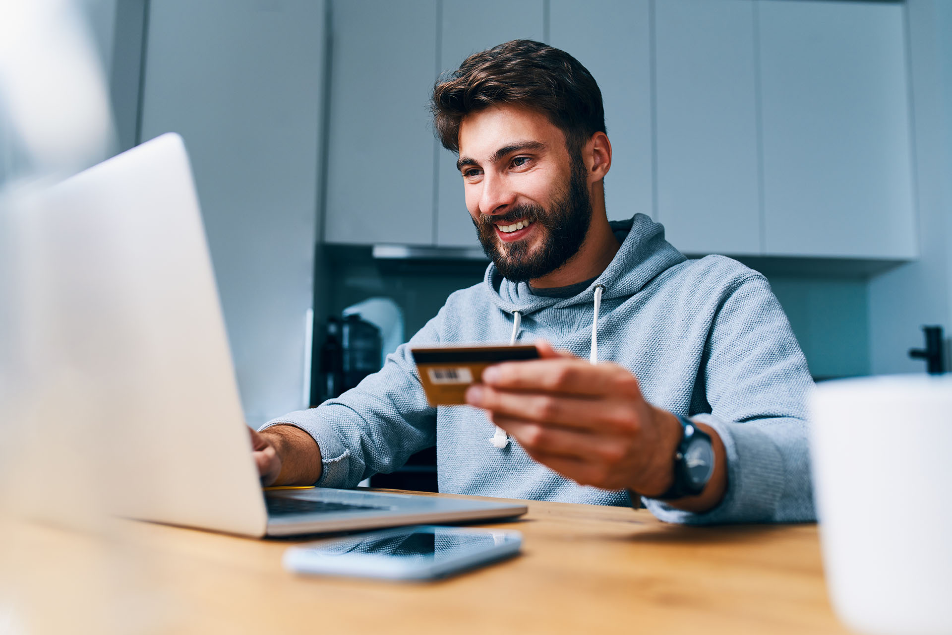 Hymyilevä mies kannettavan tietokoneen ääressä pitelemässä maksukorttia