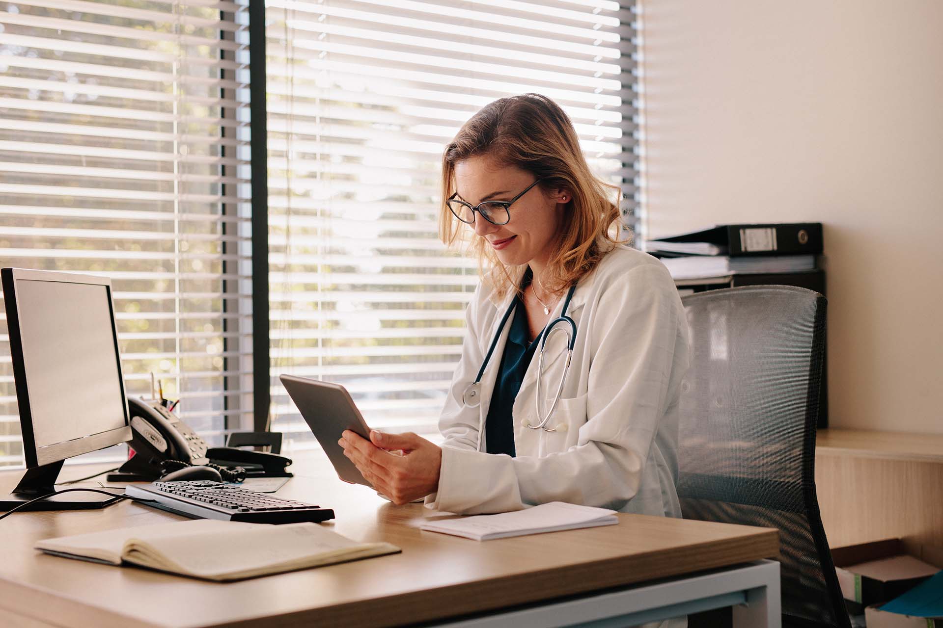 Naislääkäri istumassa työpisteellään selaamassa tablettia