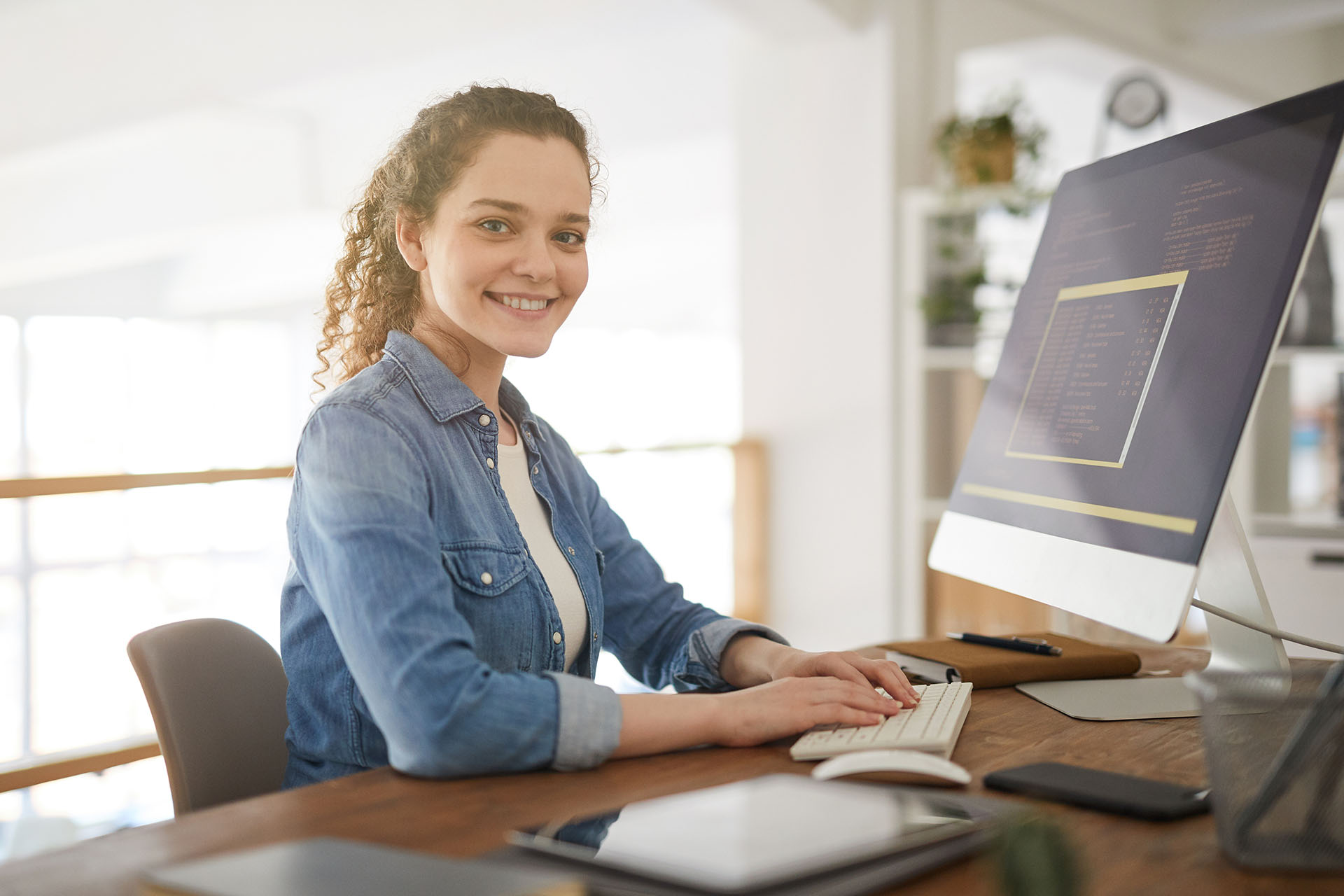 Hymyilevä nainen istumassa tietokoneen ääressä