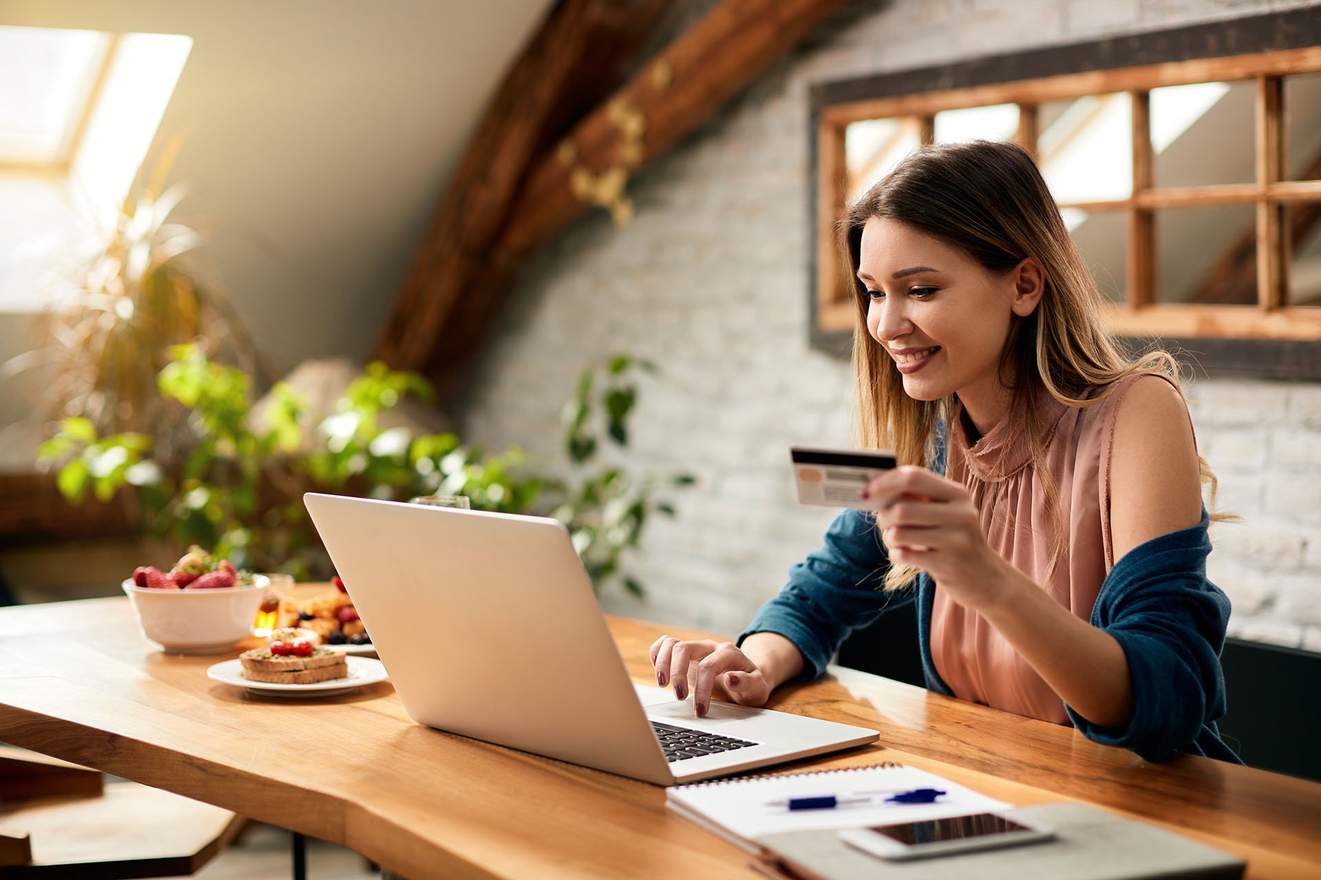 Nainen pitelemässä kädessään luottokorttia kannettavalla tietokoneella ostoksia tehdessään